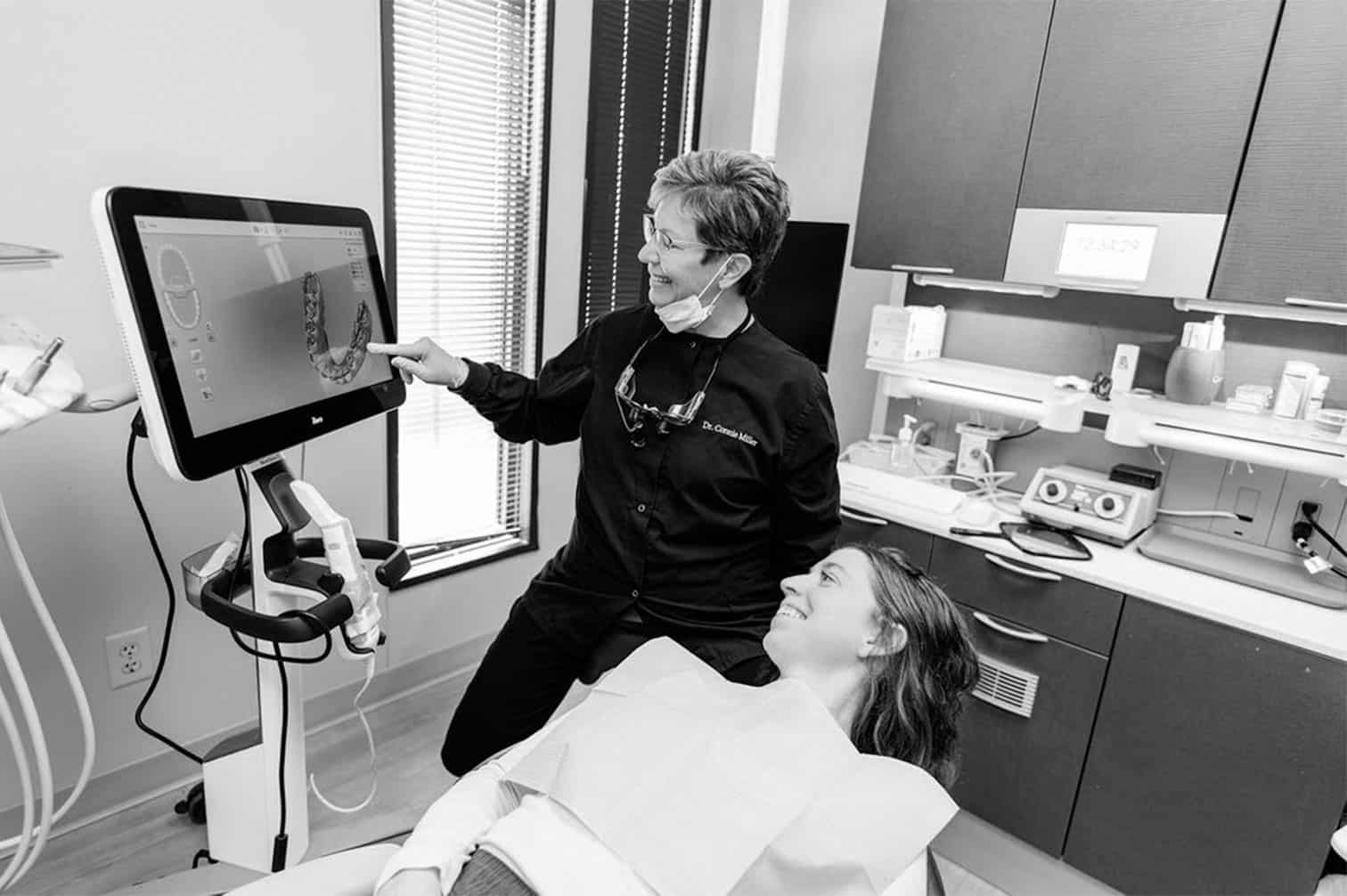 a woman sitting in a chair with a dentist pointing at a computer screen