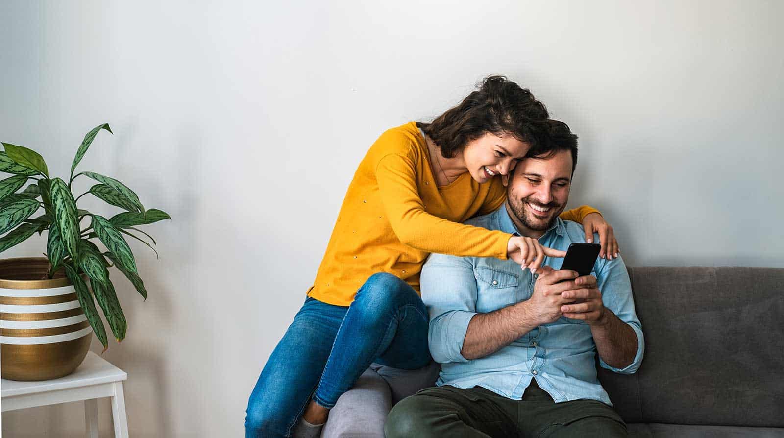 a man and woman sitting on couch and pointing at a cellphone